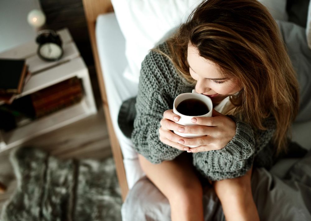 perempuan minum kopi di tempat tidur