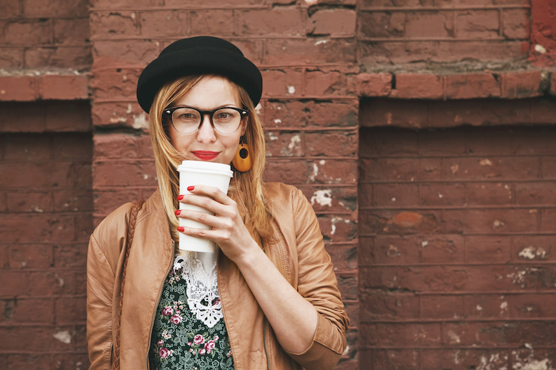 perempuan dengan topi hitam menikmati kopi dari cangkir kertas