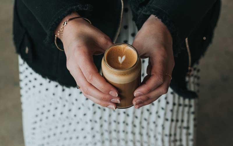 secangkir kopi latte yang dipegang dengan kedua tangan