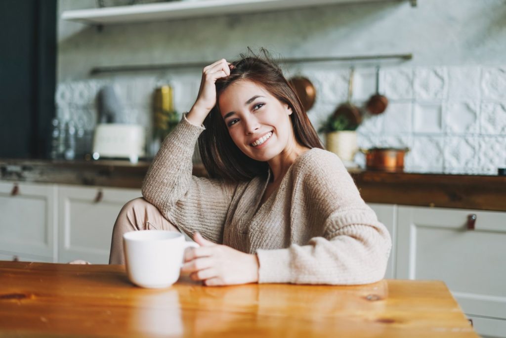 Seorang wanita bersantai di meja makan sambil menikmati kopi yang sudah dibuat oleh alat kopi dia.